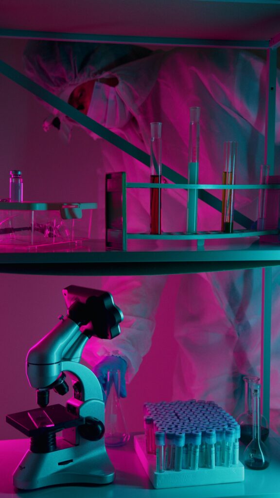 A scientist in protective gear works in a neon-lit laboratory with test tubes and a microscope.